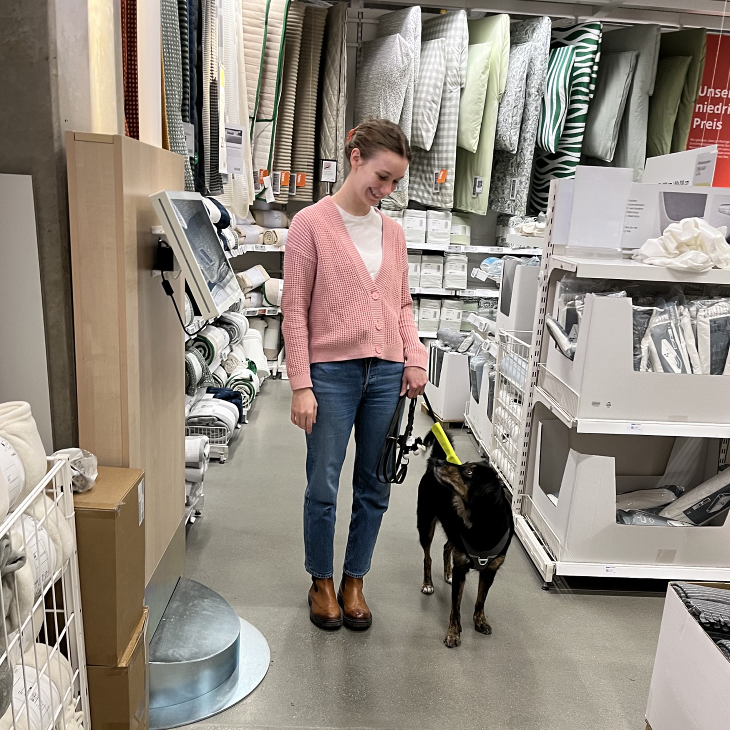 Frau steht mit Hund in einem Geschäft und die Frau lächelt den Hund an.